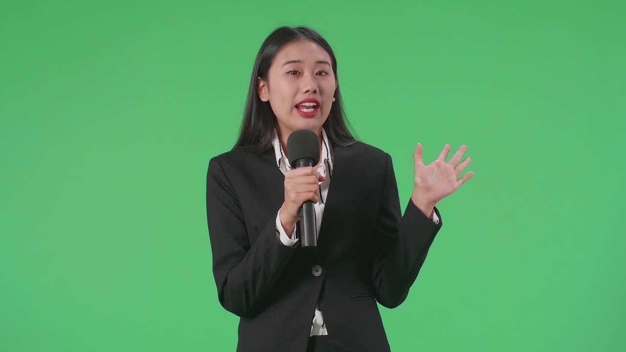 Asian Woman Journalist Pointing On Something While Speaking Into A Microphone On The Green Screen