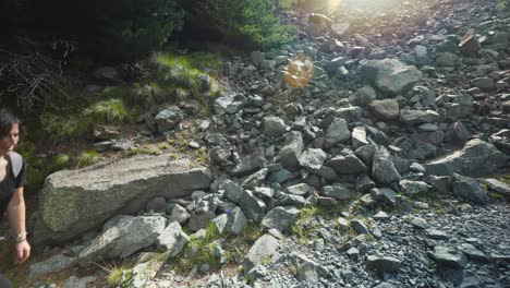 Backlit-female-hiker-with-backpack-walking-on-rocky-path,-sunny-sunset