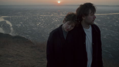 melancholic couple standing together on frozen lake shore at sunset