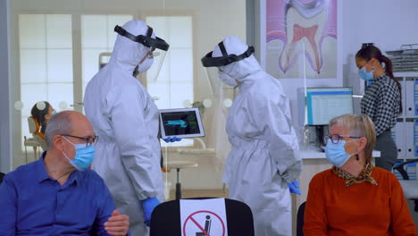 man discussing with nurse in dental reception wearing protection suit