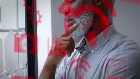 múltiples iconos digitales rojos contra pensativo afroamericano hombre de negocios sénior en la oficina