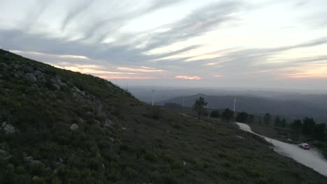 gravel road leading around a mountain with huge windmills rotating in the wind at sunset