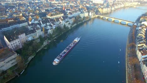 stunning sunrise captured by a drone: a cargo ship in the rhine river, leaving behind the bridge after emerging from it, moving forward in the morning light of basel, switzerland