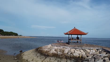 sanur beach pagoda gazebo in bali indonesia, blue sky and sea water, dock, boats in warm afternoon weather, clear sky, calm peaceful vibes