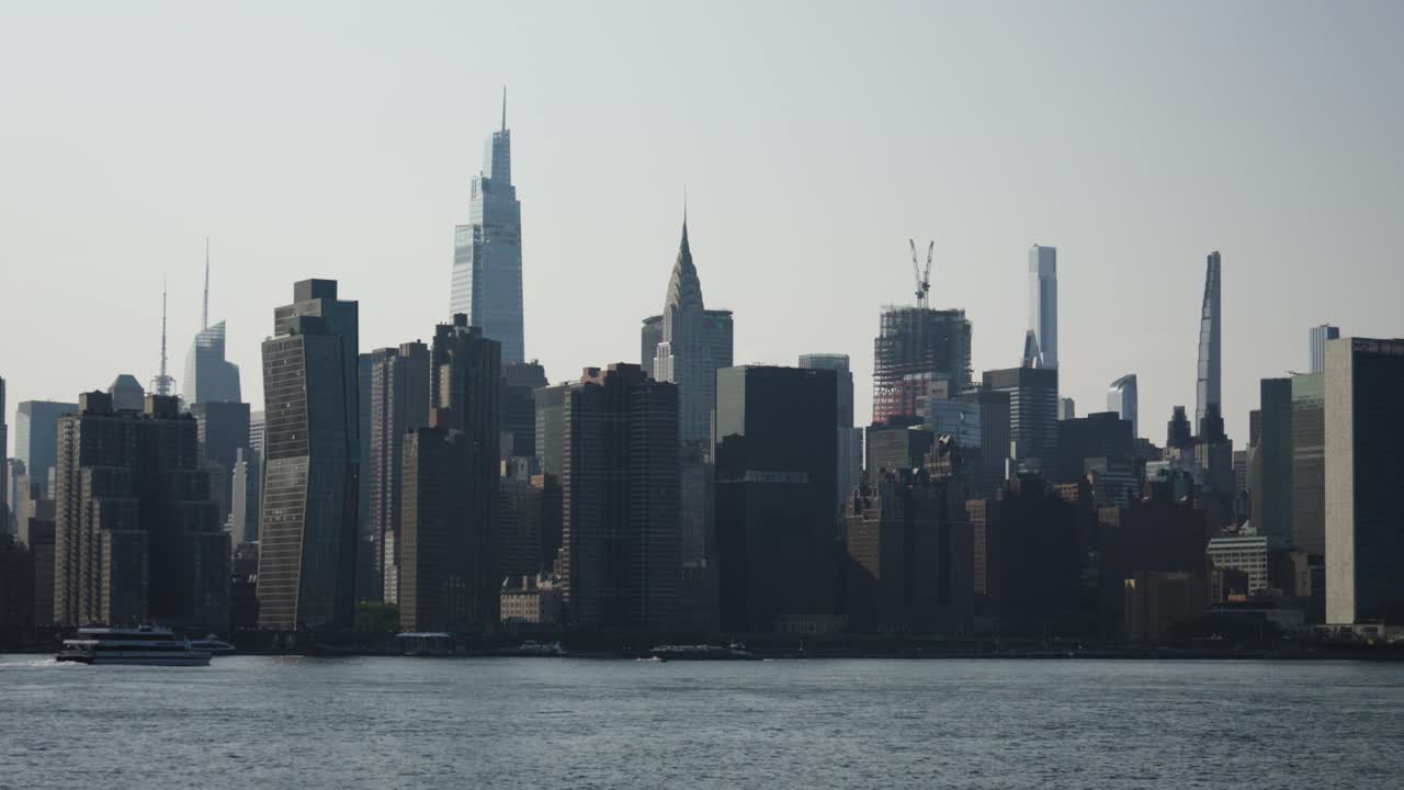 Majestic New York skyscrapers such as the Chrysler Tower and One Vanderbilt look on as a luxury riverboat yacht slices through the river's glimmer