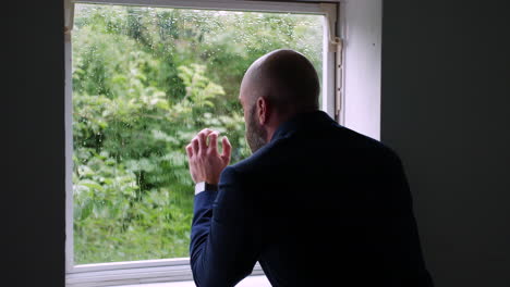 a depressed lonely businessman looking isolated in an office as he looks out of the window at the rain