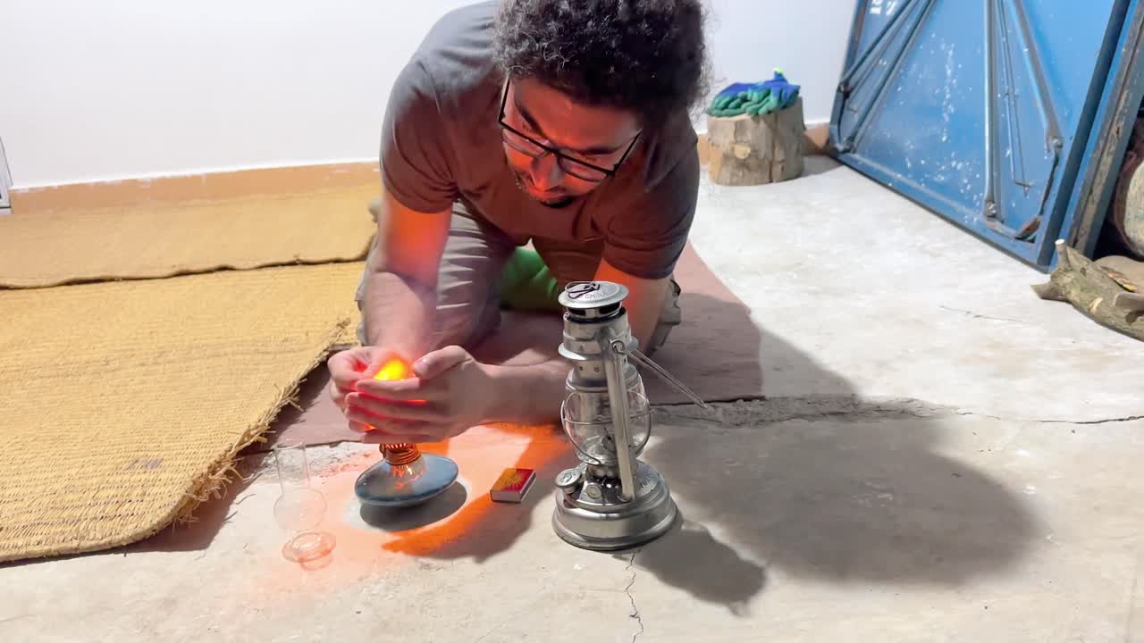 un hombre está tratando de encender una lámpara de linterna luz de aceite con fósforos la mecha empapada en aceite recipiente de arcilla azul turquesa brillante vidrio limpio en el balcón por la noche área rural vida del pueblo en el campo lado iran