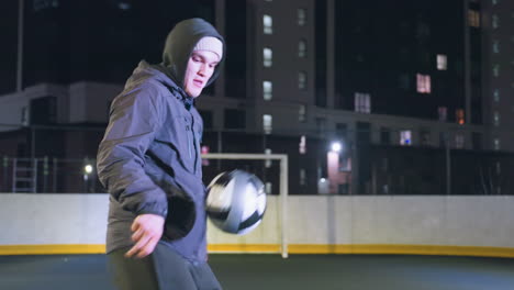 vista lateral de un futbolista corriendo hábilmente durante la práctica nocturna en un campo deportivo urbano, iluminado por farolas, contra un telón de fondo de un edificio alto