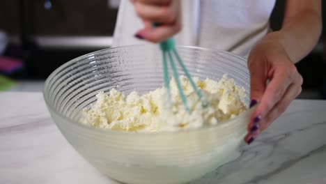 close up view of female hands preparing dough mixing flour with other ingredients using whisk in the kitchen. homemade food