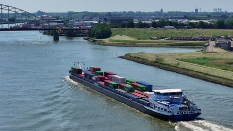 Aerial-drone-circling-around-large-cargo-ship-carrying-shipping-containers-approaching-bridge