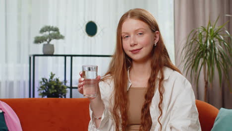 Thirsty-one-teen-girl-sitting-at-home-holding-glass-of-natural-aqua-make-sips-drinking-still-water