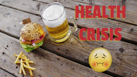 health crisis text and  nauseated face emoji against beer, burger and fries on wooden surface