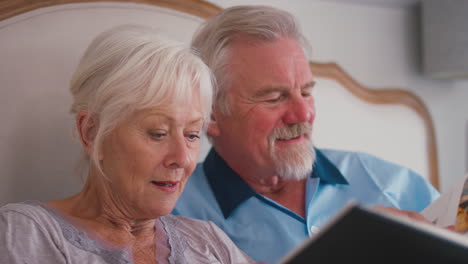 close up of retired senior couple in bed at home looking at photo album together