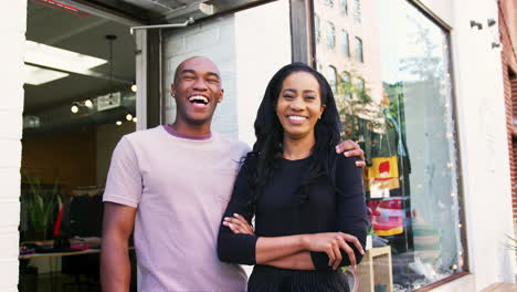 Young-couple-smiling-to-camera-outside-their-clothes-shop