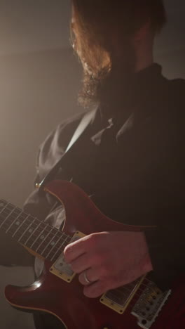 guitarist in a black outfit playing a red guitar with expressive emotion, lit by a single spotlight in a dark room
