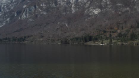 A-pan-of-the-mountains-next-to-the-lake,-surrounded-by-a-forest-on-a-cloudy-day