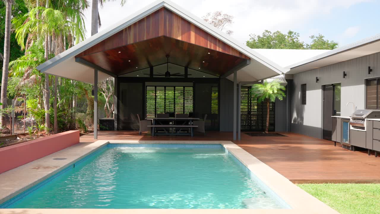 Spacious backyard of a modern tropical home with a pool and patio, surrounded by lush greenery for outdoor relaxation.