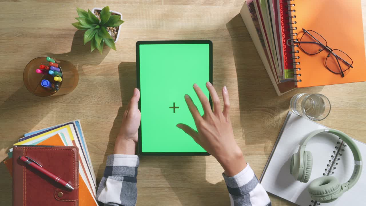 vista de arriba hacia abajo de una computadora portátil con pantalla verde simulada pantalla chromakey en un escritorio de oficina de madera al lado de la libreta con bolígrafos, gafas y un vaso de agua.