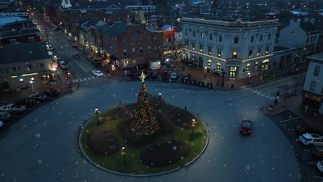 snowflakes falling on small historic town in usa with christmas tree and decorations at night