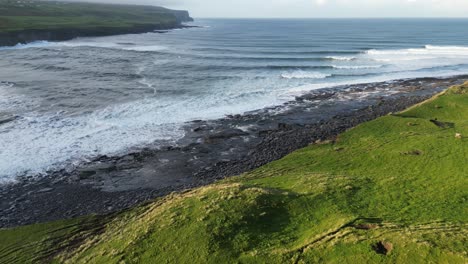 tomada aérea de un conjunto de olas que se estrellan en la playa de doolin, irlanda