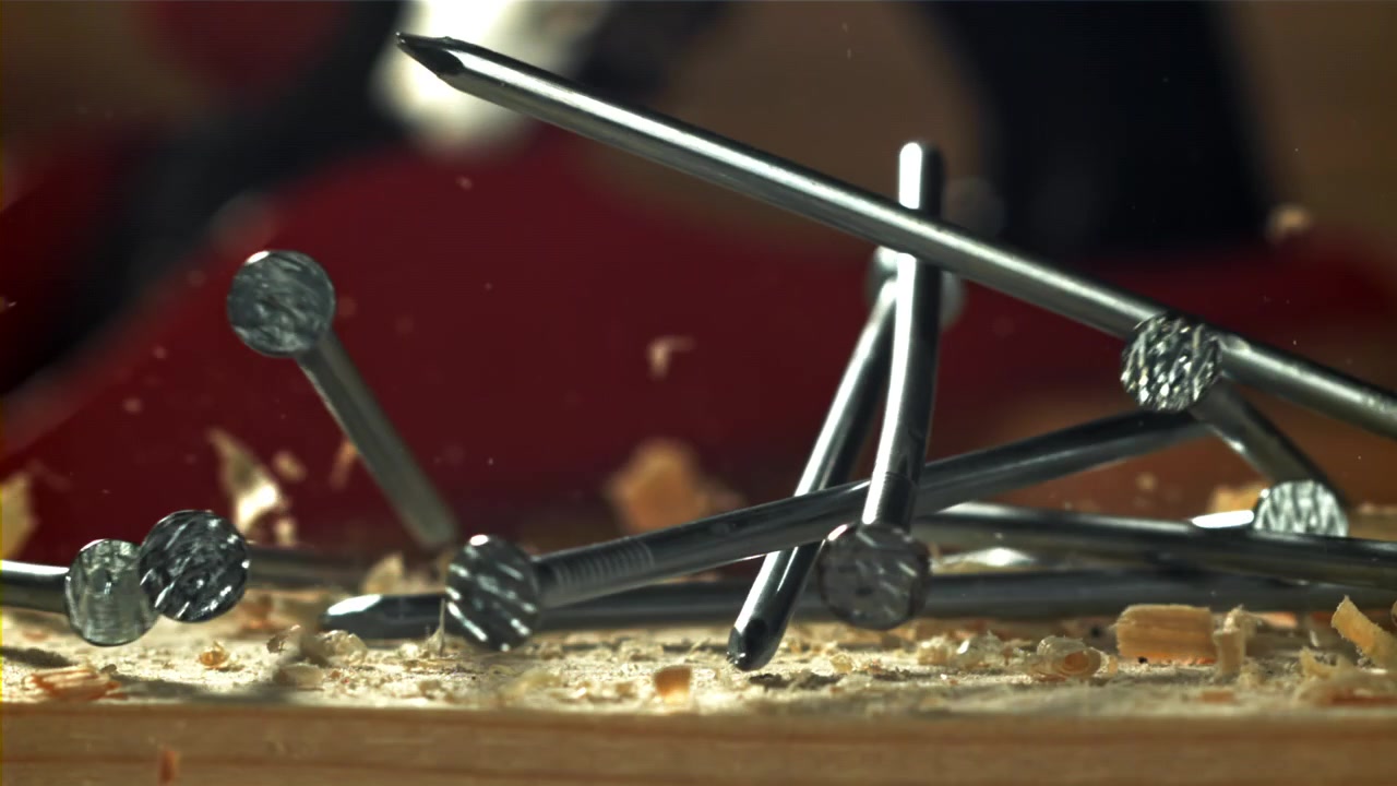 Chiodi che cadono al rallentatore su una superficie di legno con segatura