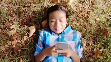 portrait of smiling girl lying on grass and using mobile phone