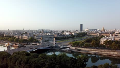 drone tour of hotel des invalides at distance from grand palais over senine river at sunrise, featuring pont alexandre iii with montparnasse tower in the background