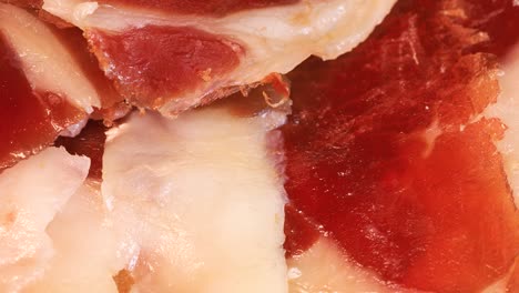 slices of intense spanish serrano ham with bread rotating on wooden board, close up view from above