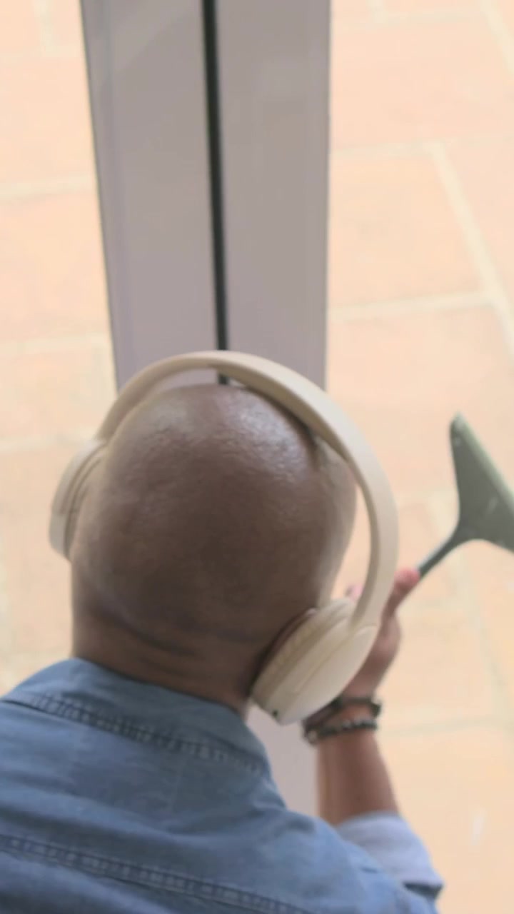 Video verticale: Uomo vestito di jeans con le cuffie indica la porta-finestra, regolando il cordino per aprirla.