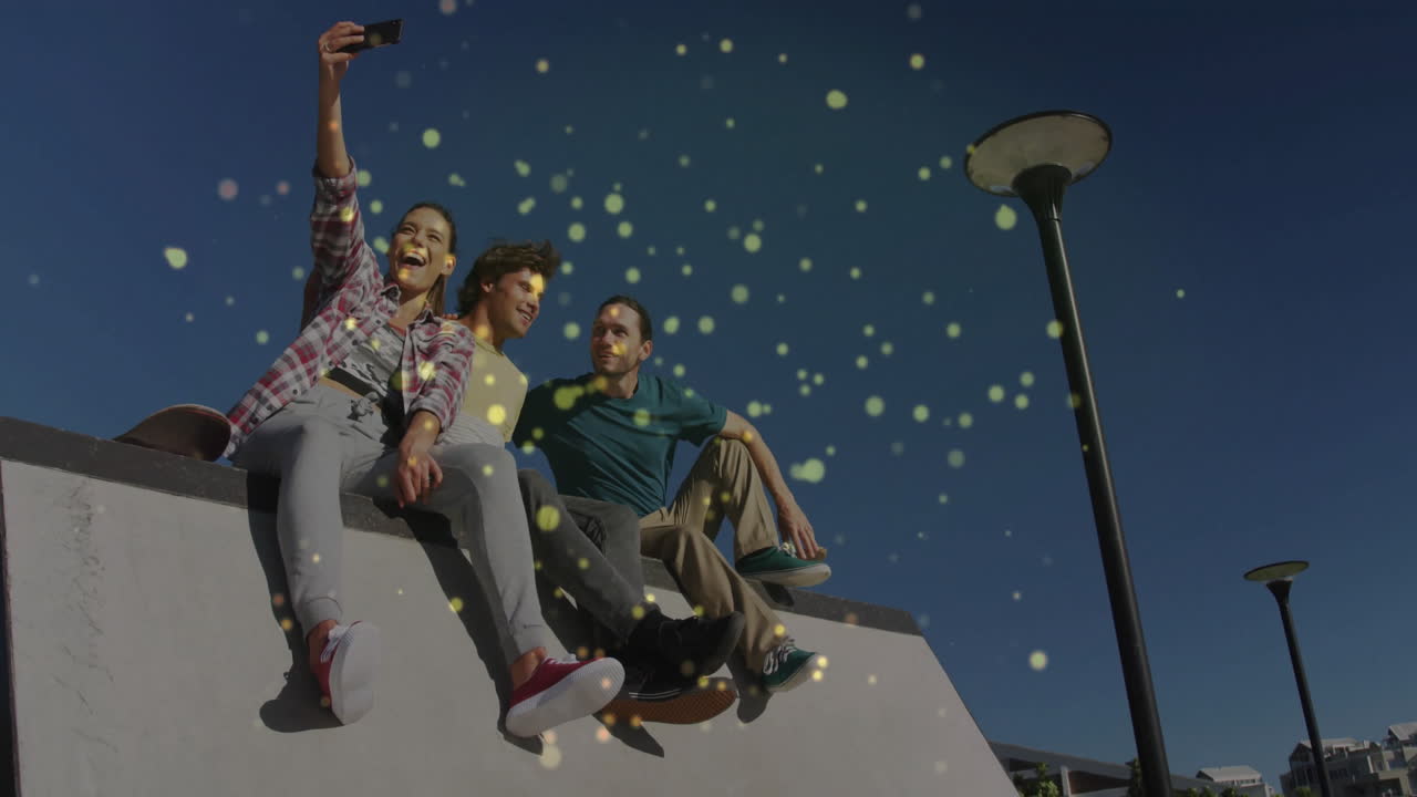 Three friends sitting on ledge in plaza, taking selfie with glowing marketing icons overlay