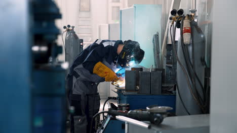 vinnytsia, ukraine - january 19, 2023: young man welder in uniform, welding mask and welders leathers, weld metal with arc welding machine at construction site, blue sparks fly to sides