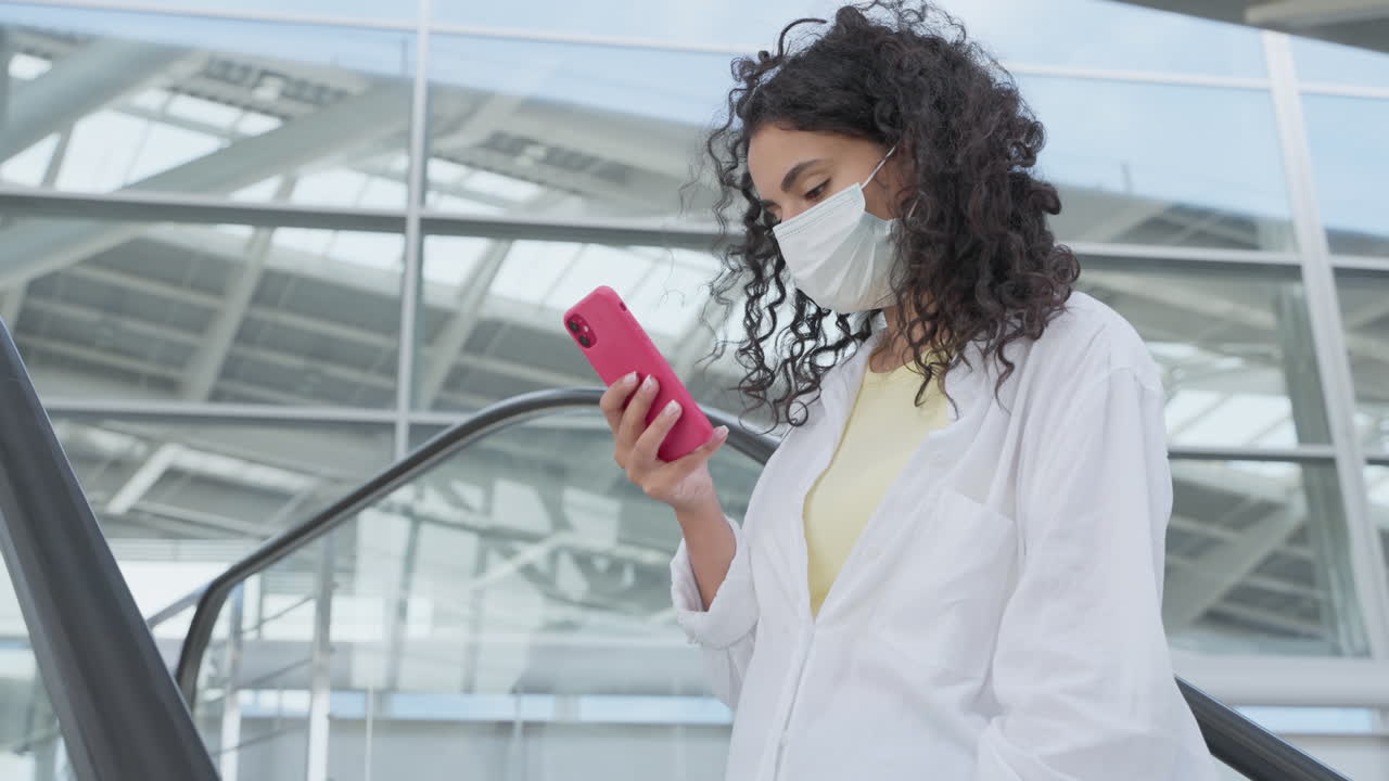 mujer con máscara mirando el teléfono en la escalera mecánica
