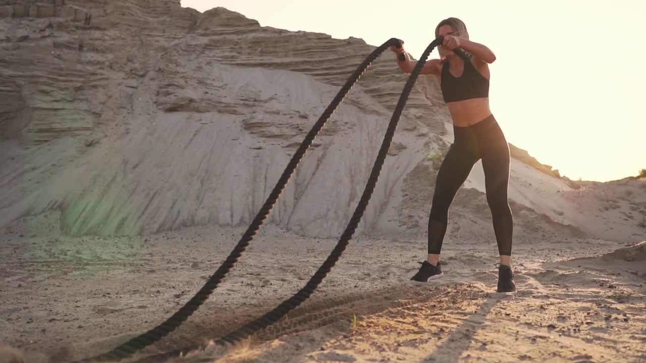 atleta entrenando al aire libre alrededor de las colinas de arena al atardecer. ejercicio de actividad física activa. crossfit. la niña tiene una cuerda en el suelo