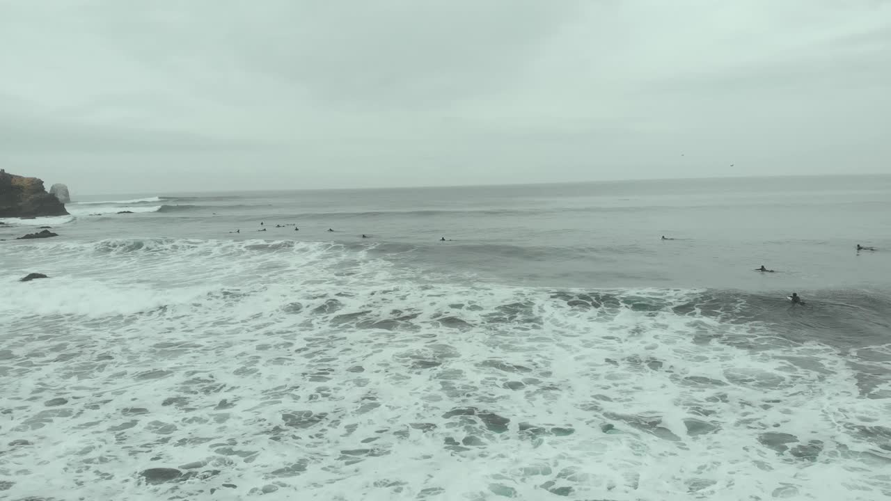 Aerial going backward over surfers, foam and waves on a cloudy day at the sea-4K