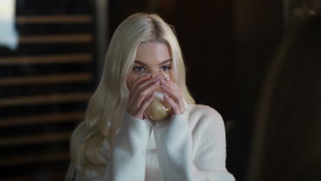 Charming-long-haired-blonde-girl-is-chatting-with-her-friend-over-a-cup-of-cappuccino-at-the-cafe