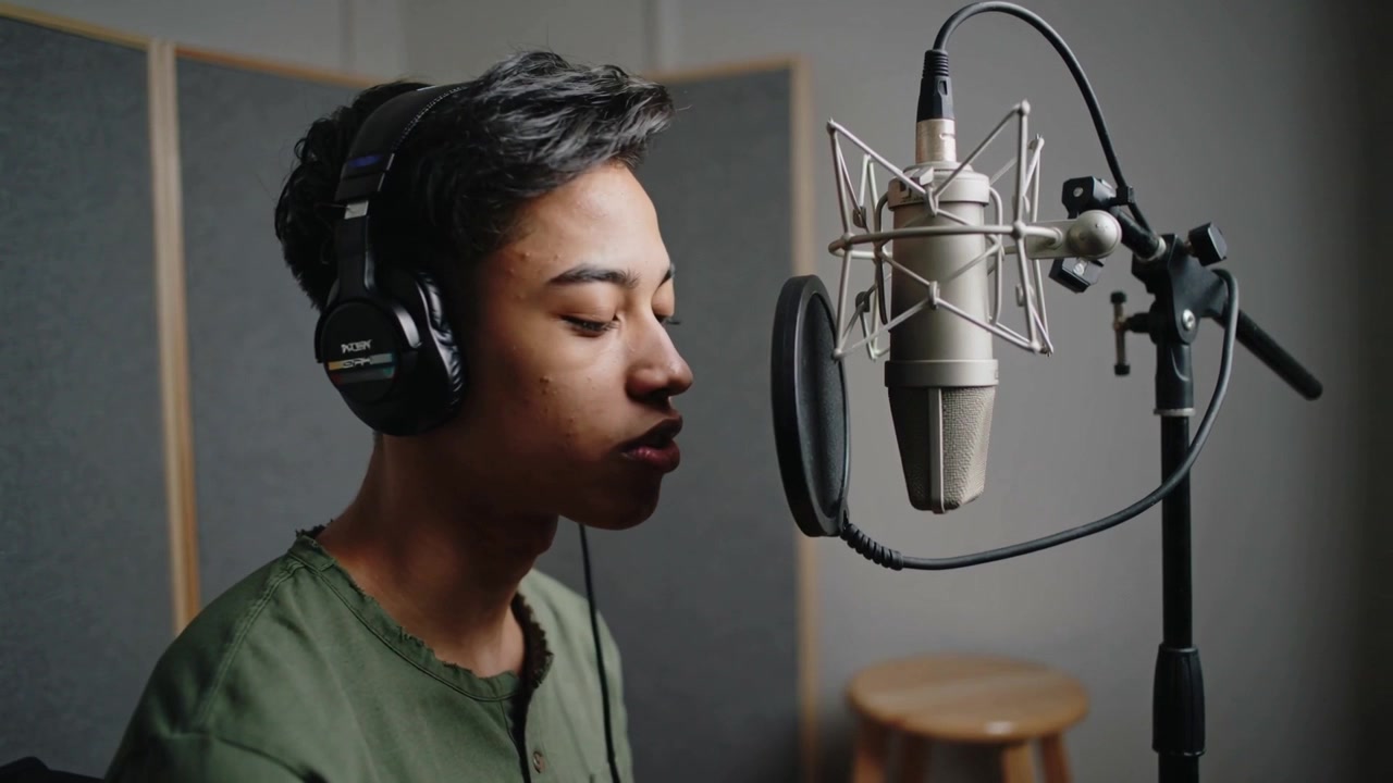 Singing vocalist in green shirt with headphones after cue for tracking in studio with condenser mic