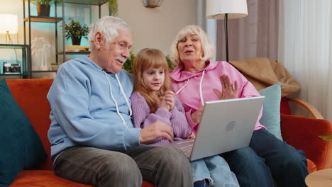 grandfather grandmother and child granddaughter making video call online on laptop at home sofa