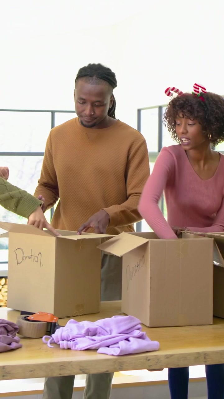 Vertical video: Picking pink hoodie, brown-sweater man sorting packing marking donation box at home