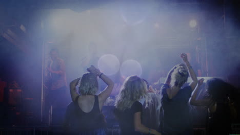 concert audience dancing under purple-blue lights, musician singing into mic, smoke swirling