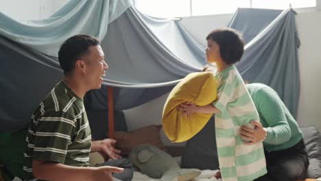 아시아 젊은 아버지는 딸과 함께 베개를 던지며 놀고, 어머니는 웃으며, 행복한 가족은 집에서 재미있게 놀고 있습니다.