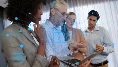 Animation-of-dots-around-padlock-in-shield-over-diverse-coworkers-discussing-reports-on-laptop