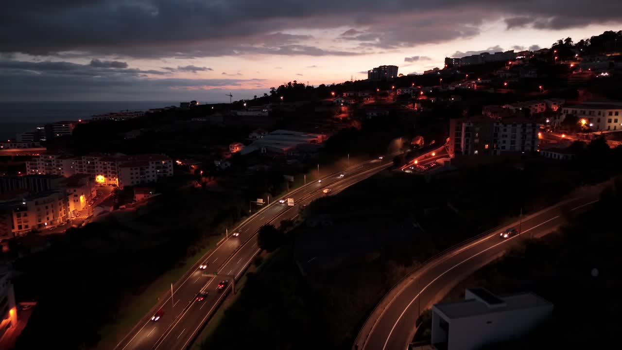 Canico town at night with glowing streetlights and buildings illuminated on Madeira coastline, aerial view road journeys