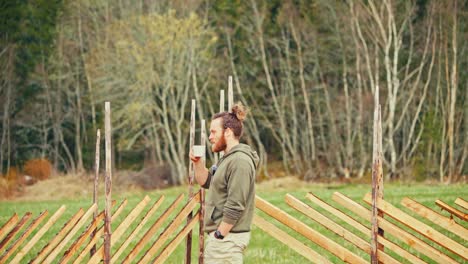 bearded norwegian guy drinking coffee while standing near skigard wooden fence. static shot