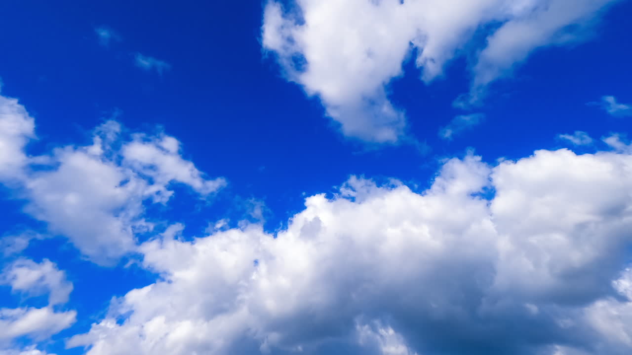 Soft fluffy white clouds flying in the atmosphere. Low angle view on the cloudscape covering the blue sky. Timelapse.