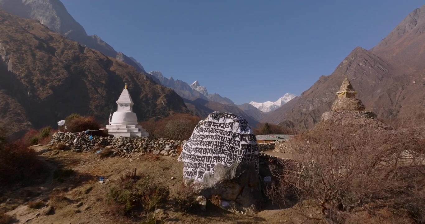 Phortse village, Khumbu Region, Everest Nepal, aerial drone glide in shot toward traditional white and stone Buddhist stupas and a large carved mani stone with snow-capped mountain peaks