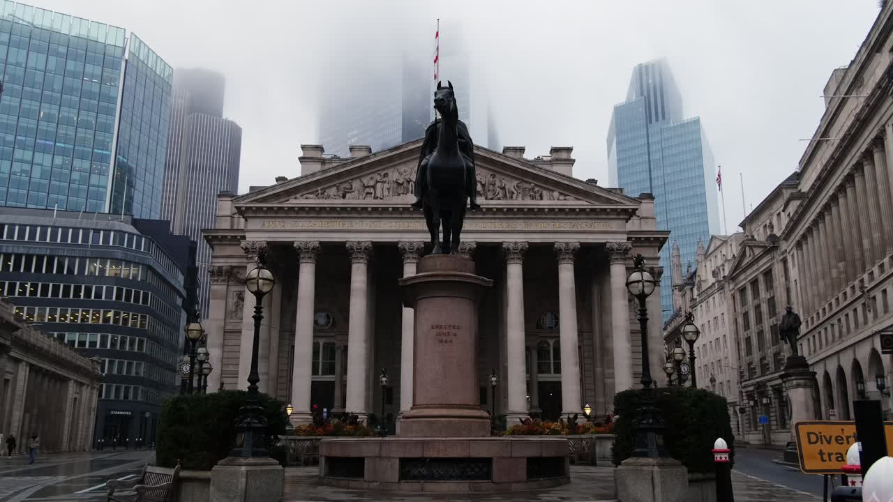 Bank of England and Royal Exchange In City Of London With Skyscrapers In Background during a misty and rainy morning.