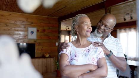 Feliz-Pareja-Afroamericana-Mayor-Abrazándose-Y-Mirando-Por-La-Ventana-En-Casa,-Cámara-Lenta