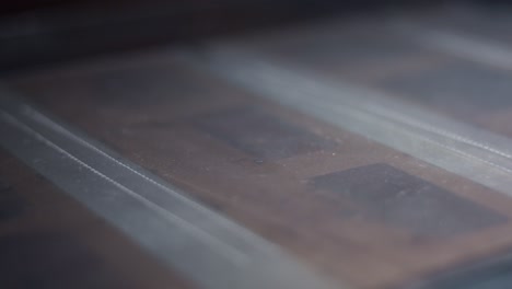 a hand with a magnifying glass carefully examines the negatives of the photos