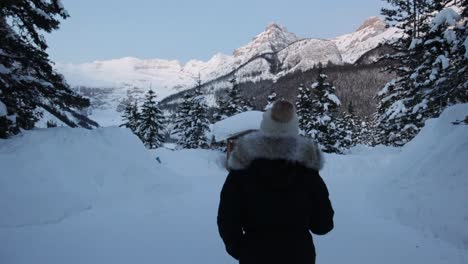 Camera-follow-person-wearing-winter-clothes-walking-on-snow,-Alpine-landscape