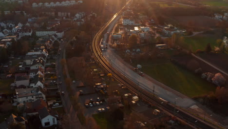 Aerial-view-on-railway-double-track-line-passing-through-outskirts-of-small-town.-Tilt-up-footage-reveals-setting-sun.-Pleasant-evening-atmosphere.-Bad-Vilbel,-Germany.